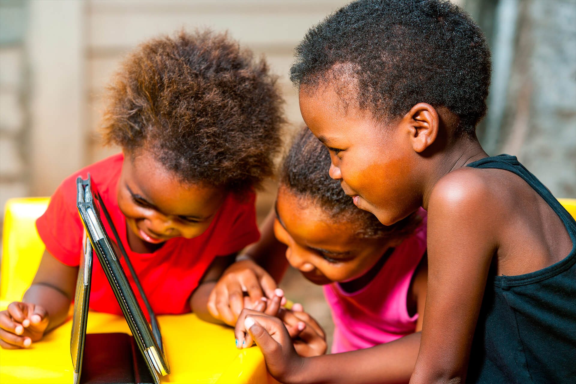 Three young children sharing a tablet together outdoors