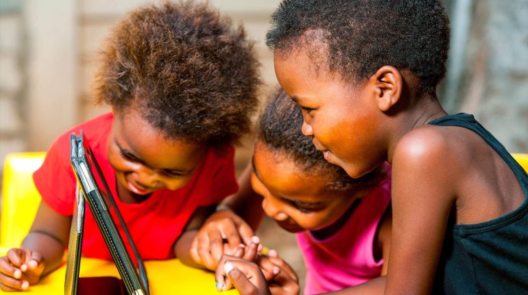 Three young children sharing a tablet together outdoors