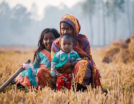 A mother and her two children sitting together in a harvested field